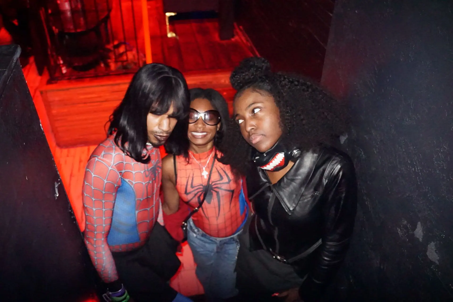 Three friends posing in a red stairwell, two in Spider-Man looks